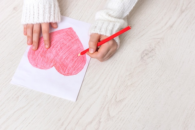 Las manos del niño se cierran dibujando un corazón rojo sobre un fondo claro. Copiar espacio para texto