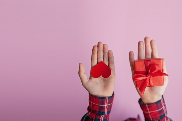 Manos del niño con corazón de papel rojo y caja presente en la mano. Concepto de día de San Valentín