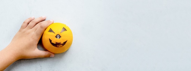 Las manos de un niño dibujando un bozal aterrador en una calabaza para la fiesta de halloween. Minimalismo. Gris y naranja.