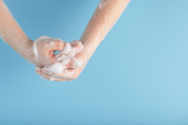 Manos de un niño en espuma antibacteriana jabonosa, en una pared azul, vista desde arriba.