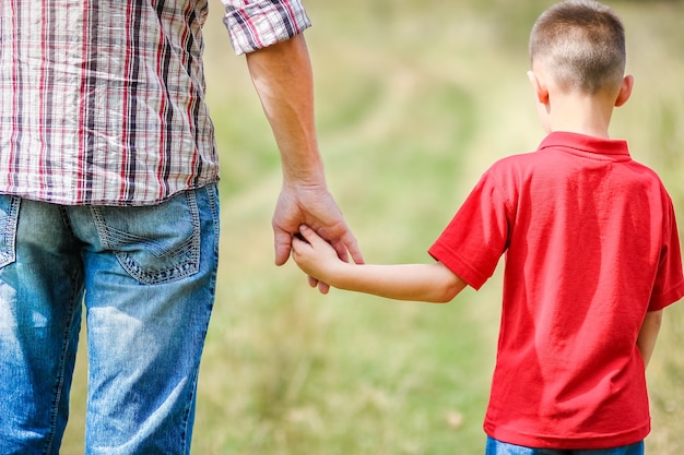 Manos de un niño feliz y un padre en la naturaleza en el concepto de familia del parque