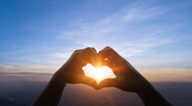 Manos de niño en forma de corazón contra el fondo del atardecer del cielo Concepto de amor