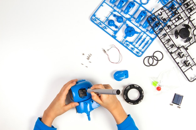 Manos de niño haciendo robot azul en el escritorio blanco.