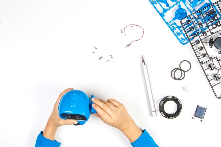 Foto manos de niño haciendo robot azul en el escritorio blanco.