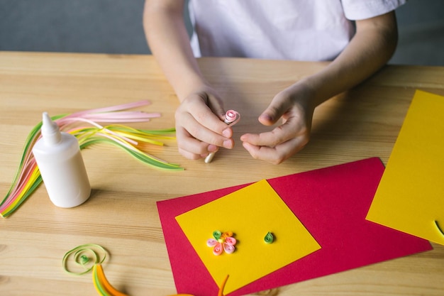 Con las manos de un niño, haga una tarjeta de quilling, gire una tira de papel rosa con un punzón