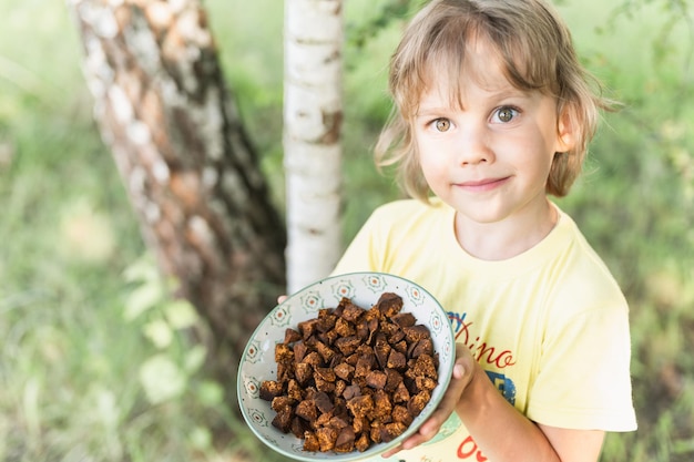 Manos de niño niño feliz sosteniendo la placa con piezas de chaga limpias y cortadas. Seta chaga forrajeada hongo de abedul silvestre se usa en medicina alternativa para preparar té curativo para el tratamiento covid-19