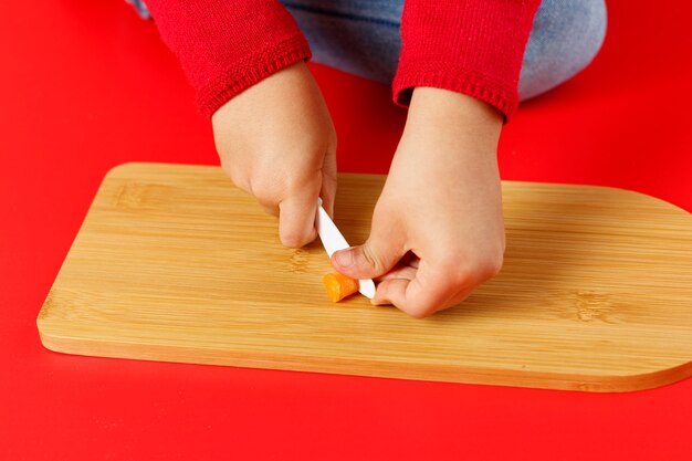 Manos de niño pequeño cortando zanahorias en la mesa