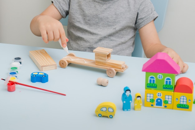 Las manos de un niño pintan una máquina de madera.