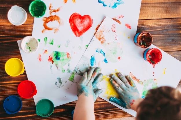 Manos de un niño pintando mosaico de colores El niño está dibujando en hojas blancas con pinturas de dedos