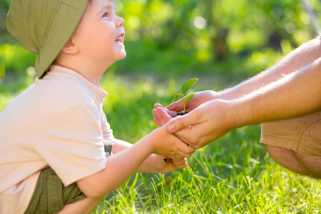 Foto manos de un niño que toma una planta de las manos de un hombre. concepto eco día de la tierra