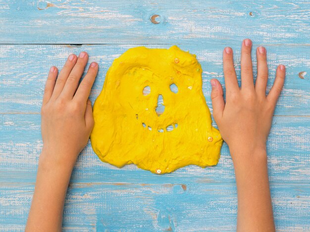 Las manos del niño sobre la mesa junto a la cara de un limo amarillo. Juguete antiestrés. Juguete para el desarrollo de la motricidad manual.