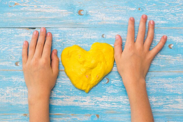 Las manos del niño sobre la mesa con limo amarillo en forma de corazón. Juguete antiestrés. Juguete para el desarrollo de la motricidad manual.