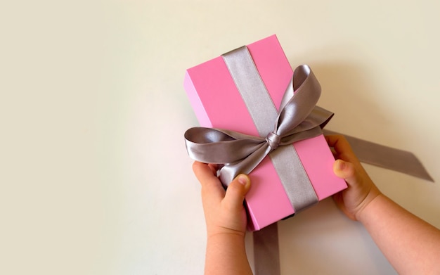 Manos de niño sosteniendo caja de regalo rosa con lazo plateado