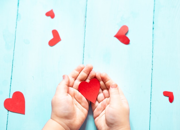 Las manos de un niño sosteniendo un corazón rojo sobre un fondo azul.