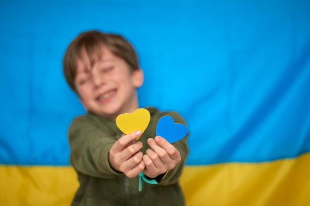 Manos de niño sosteniendo corazones de papel amarilloazul sobre fondo de bandera ucraniana