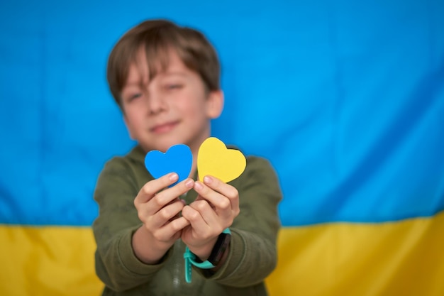 Manos de niño sosteniendo corazones de papel amarilloazul sobre fondo de bandera ucraniana