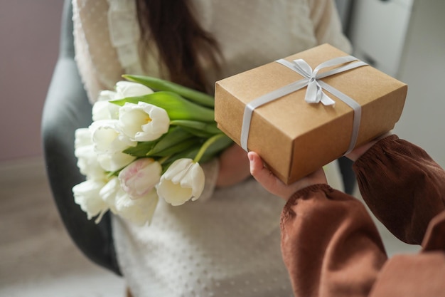 Las manos del niño sostienen una hermosa caja de regalo con una cinta y tulipanes blancos Primer plano de vista superior Feliz día de la madre