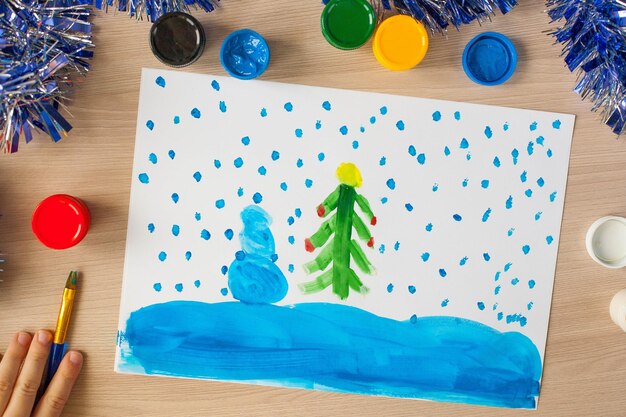 Las manos del niño sostienen un pincel y toman gouache de un frasco Pasatiempos y entretenimiento para niños Primer plano Dibujo de un árbol de Navidad