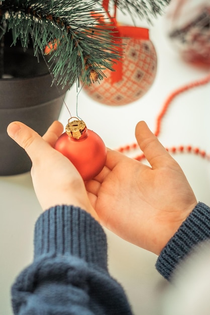 manos de un niño en un suéter de Navidad sostienen una decoración de árbol de Navidad