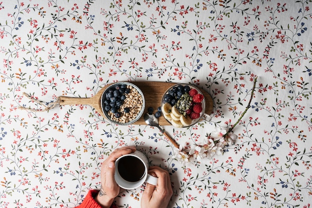 Las manos de un niño con una taza de café y yogur con frutas en una cama