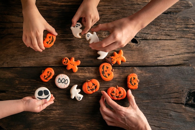 Las manos de los niños alcanzan el pan de jengibre de Halloween en forma de calabazas fantasmas y hombre de pan de jengibre sobre fondo de madera