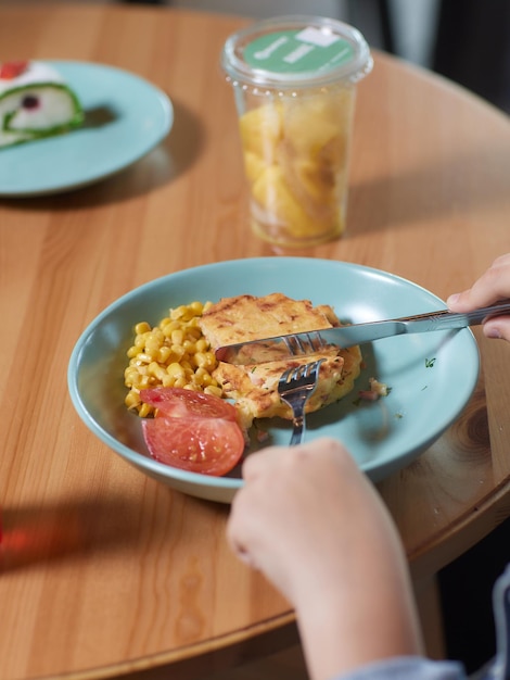 Las manos de los niños cortan con un cuchillo y sujetan con un tenedor un gran trozo de carne de cerdo picada