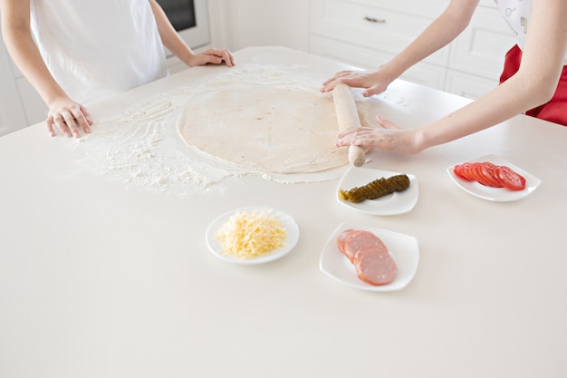 Las manos de los niños despliegan la masa de pizza sobre una mesa blanca. Divirtiéndose juntos en la cocina. Vista desde arriba.