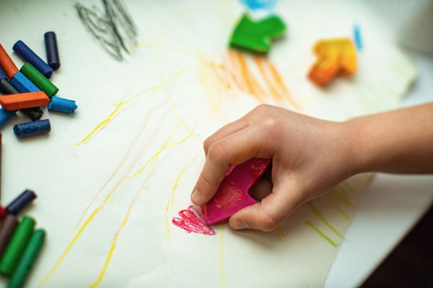 Las manos de los niños dibujan con lápices de cera caseros a partir de fragmentos de crayones viejos