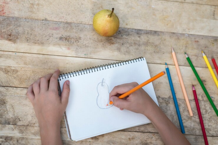 Foto las manos de los niños dibujan una pera con lápices de colores. vista superior