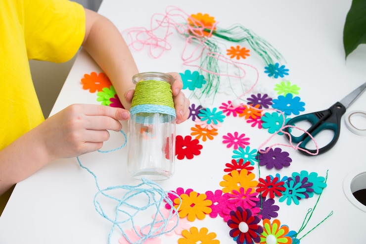 Foto las manos de los niños envuelven el hilo alrededor de un frasco de vidrio para hacer artesanías en casa