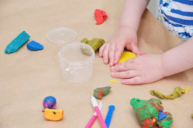 Las manos de los niños esculpen un círculo de plastilina amarilla, una niña juega con plastilina en la mesa