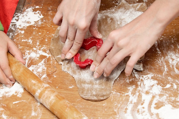 Las manos de los niños extienden la masa para pan de jengibre. Primer plano de las manos.