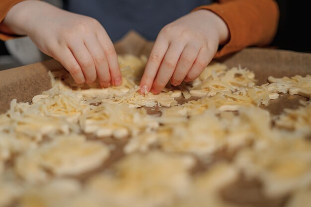 las manos de los niños hacen galletas de queso en una bandeja de metal con pergamino