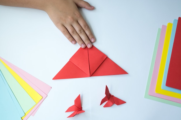 Las manos de los niños hacen origami una mariposa.