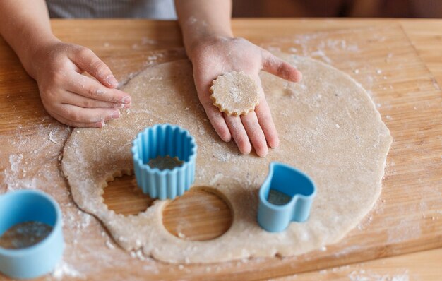 Manos de los niños haciendo galletas de jengibre en una mesa de madera.