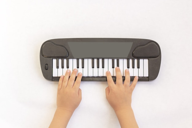 Las manos de los niños juegan en las teclas del piano, sintetizador de juguete sobre fondo blanco.