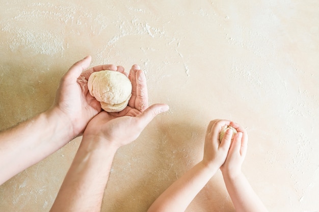 Las manos de los niños y de papá hacen masa cruda