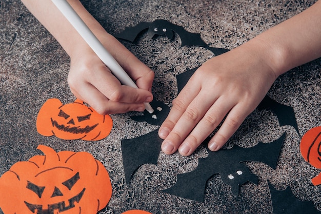 Las manos de los niños preparan decoraciones de papel para Halloween Preparándose para las vacaciones