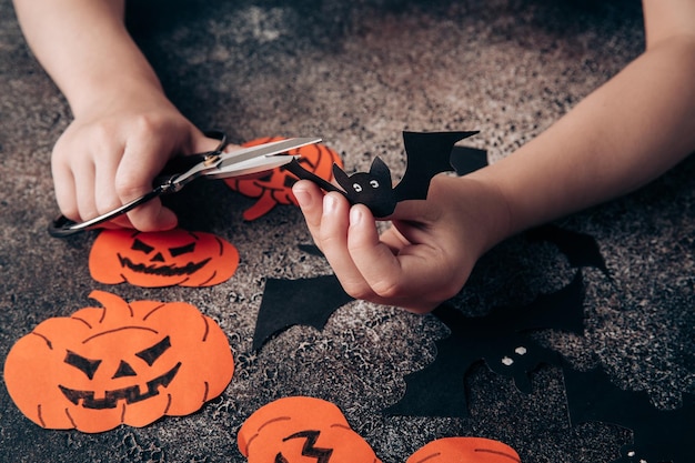 Las manos de los niños preparan decoraciones de papel para Halloween Preparándose para las vacaciones