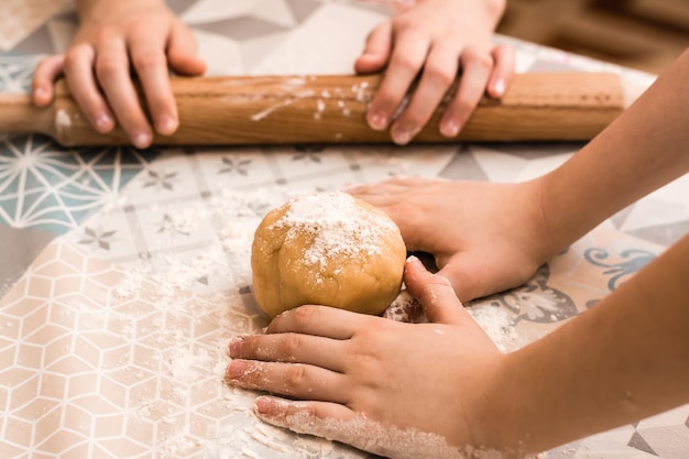 Las manos de los niños se preparan para usar un rodillo para enrollar masa de jengibre para hornear galletas Linzer en la mesa de la cocina. Estilo de vida