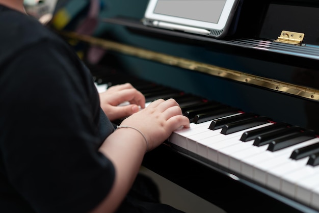 Las manos de los niños presionan la tecla del piano para aprender música en línea