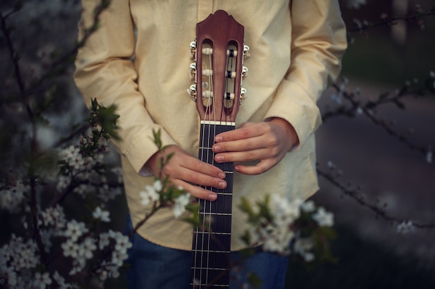 Manos de los niños que sostienen la guitarra en fondo de la naturaleza.