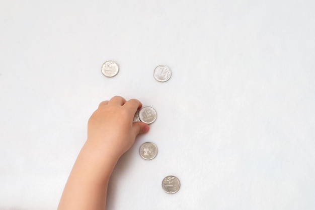 Las manos de los niños recogen monedas de un rublo ruso sobre un fondo blanco.