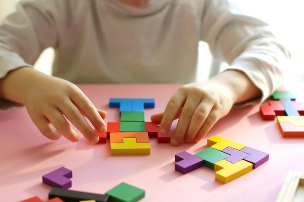 Manos de los niños con un rompecabezas de tangram de color sobre un fondo rosa, juegos infantiles cotidianos, juguetes ecológicos de madera para el ocio de los niños