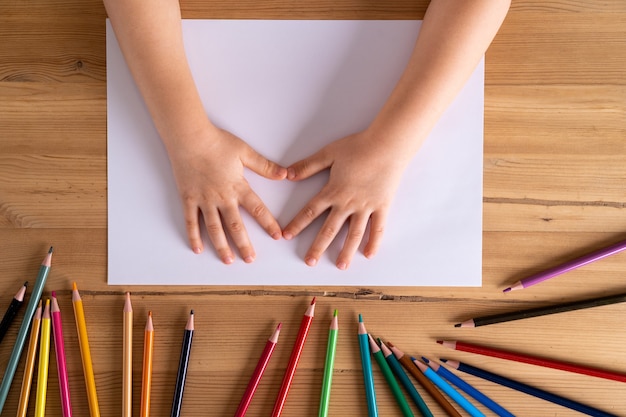 manos de los niños sobre la mesa y una hoja de papel blanco y lápices de colores, el concepto de