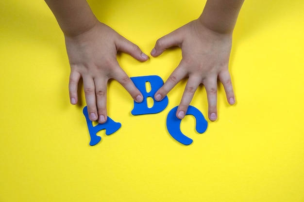 Manos de niños sosteniendo letras en un fondo amarillo