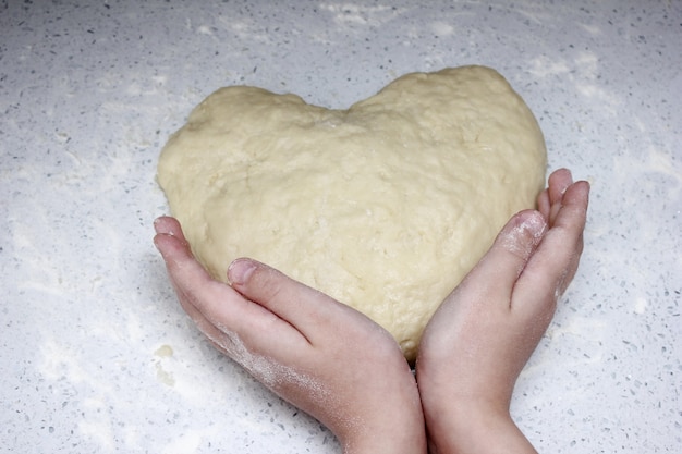 Las manos de los niños sostienen un corazón hecho de masa.