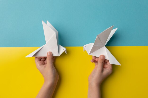 Las manos de los niños sostienen dos pájaros blancos como símbolo de paz en papel de color azul y amarillo pastel Sin guerra Detener la guerra