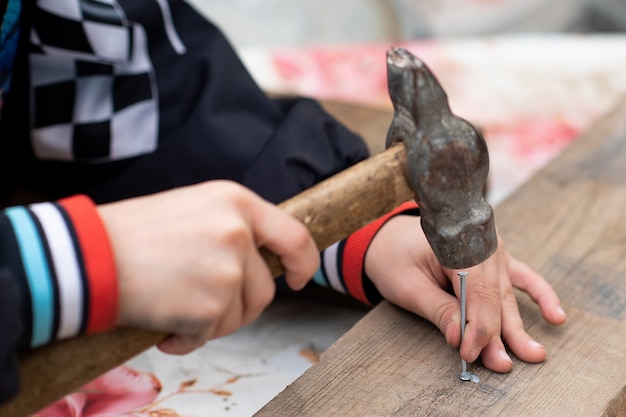 Las manos de los niños sostienen un martillo y clavan un clavo en la tabla.