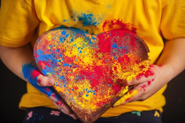 las manos de los niños sostienen un plato de madera en forma de corazón con coloridos colores Holi